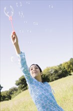 Hispanic girl making bubbles in field