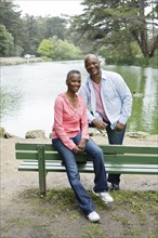 African American couple sitting on bench near lake