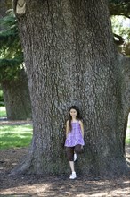 Mixed race girl leaning against tree trunk in park