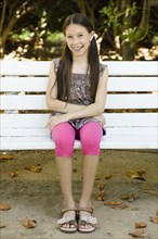Smiling mixed race girl sitting on park bench