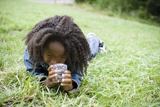 African American boy laying in grass and looking in jar