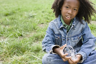 African American boy sitting in grass and holding jar