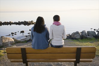 Black couple sitting on bench near shore
