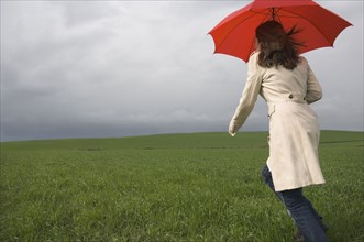 Rear view of woman running with umbrella in field