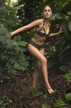 Hispanic woman wearing camouflage bikini in jungle