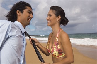 Woman pulling man's necktie at beach