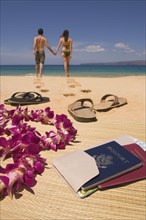 Couple walking away from passport and sandals on beach
