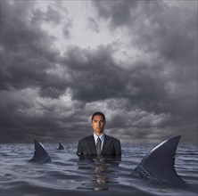 Hispanic businessman standing in water with sharks