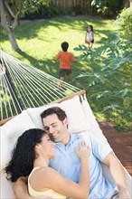 Couple relaxing in hammock with children playing in background