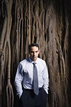 Sad Latin businessman standing near tree roots