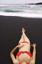 Woman sunbathing on black sand beach