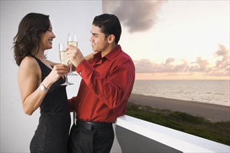 Hispanic couple toasting each other on balcony
