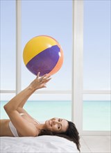 Hispanic woman holding beach ball on bed