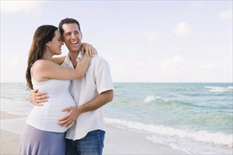 Caucasian man hugging pregnant wife on beach