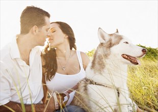 Caucasian couple sitting with dog in tall grass