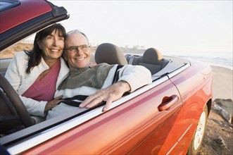 Older couple driving convertible on beach