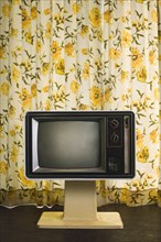 Old-fashioned television near floral curtain
