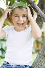 Caucasian girl sitting in tree holding leaf in hair