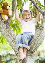 Caucasian girl sitting in tree with teddy bear