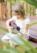Caucasian girl sitting on patio playing ukulele