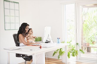 Mixed Race mother using computer and holding baby daughter