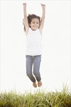 Mixed Race girl jumping for joy in grass