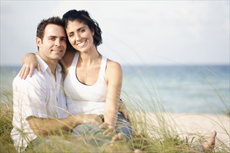 Portrait of Mixed Race couple sitting in grass at beach