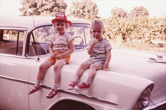 Caucasian brother and sister sitting on vintage car