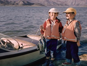 Portrait of Caucasian brother and sister posing with fish near boat