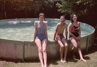 Portrait of Caucasian brother and sisters leaning on swimming pool