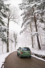 Green car driving on narrow road in winter