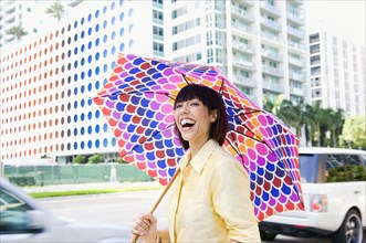 Laughing Mixed Race woman carrying umbrella in city