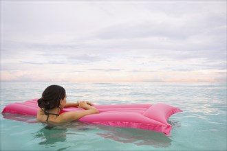 Mixed Race woman floating in ocean on inflatable raft