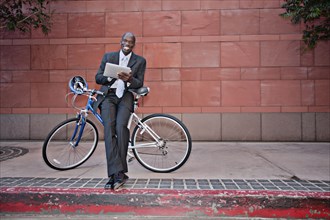 Businessman leaning on bicycle using digital tablet