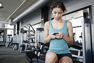 Mixed race woman text messaging on cell phone in health club
