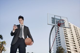 Mixed race businessman holding basketball and text messaging on cell phone