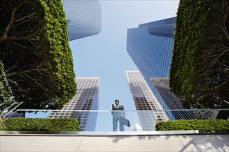 Businessman standing on balcony text messaging on cell phone