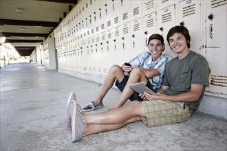 School friends leaning on lockers using digital tablet