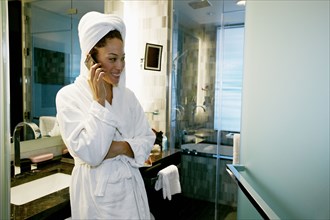 Mixed race woman talking on cell phone in bathroom