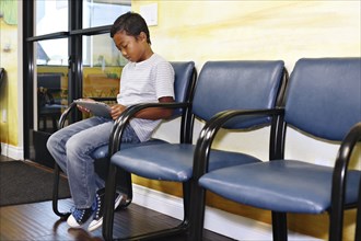 Mixed race boy using digital tablet in waiting room