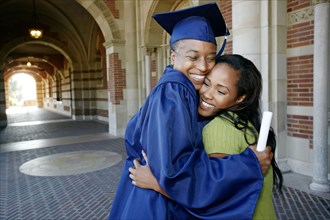 Smiling Black woman holding graduation diploma and hugging daughter