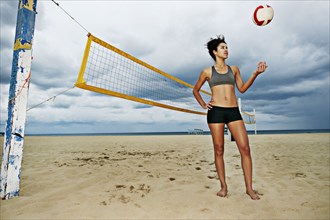 Mixed race woman playing with volleyball on beach