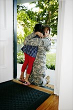 Mixed race soldier mother hugging daughter in front door
