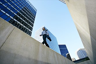 Asian businessman walking on ledge in city