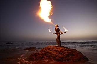 Woman breathing fire on rocky beach
