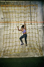 African American woman climbing net wall in gym