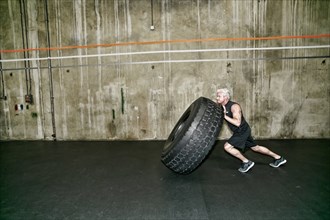 Mixed race man pushing large tire in gym