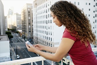Mixed race woman using cell phone on urban rooftop