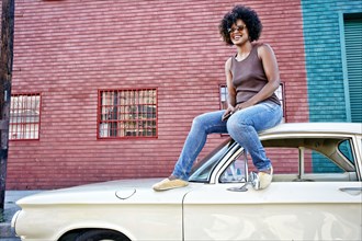 Mixed race woman sitting on vintage car