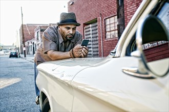 Hispanic man using cell phone on vintage car